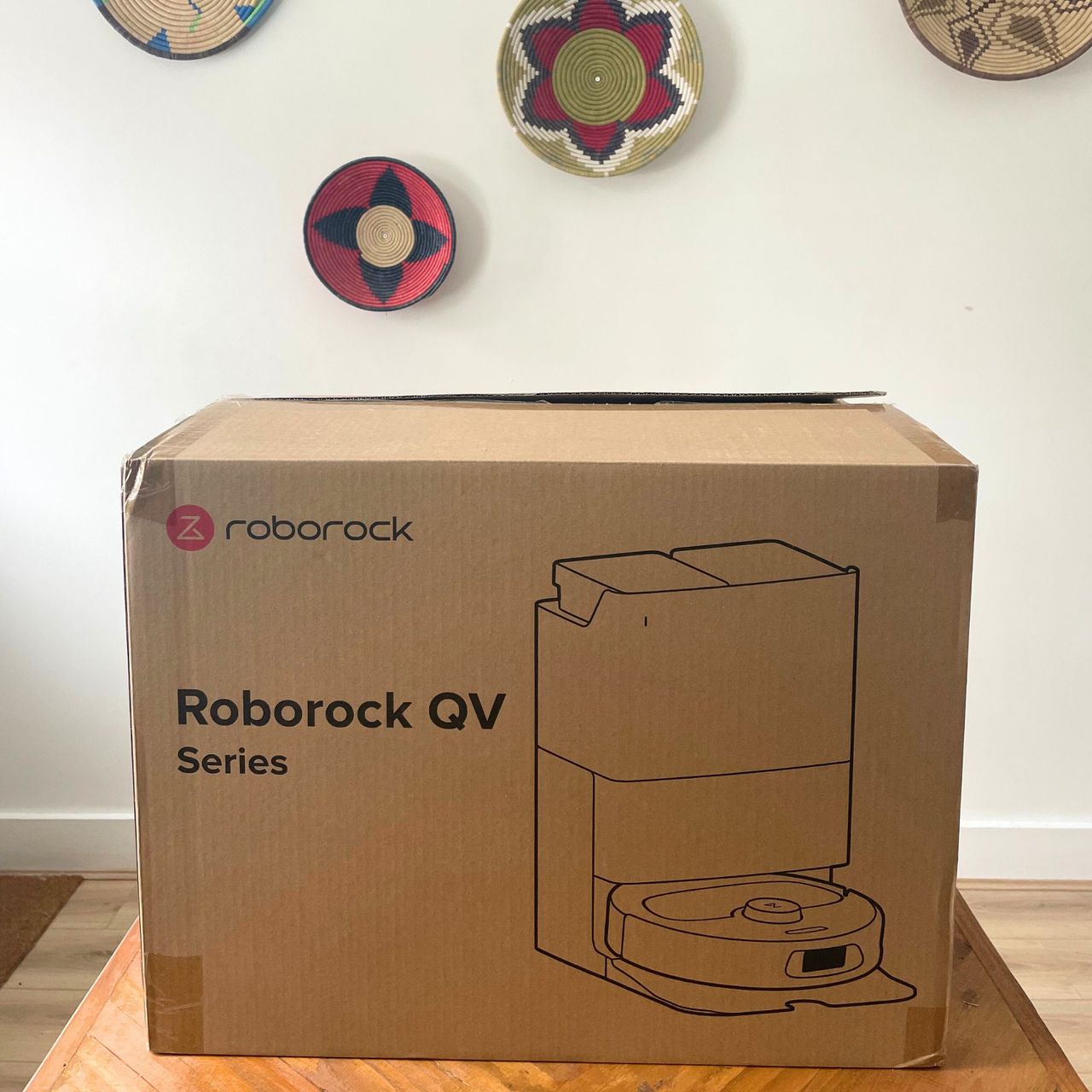 Roborock QV 35S Robot Vacuum box on a wooden table, in front of a white painted wall
