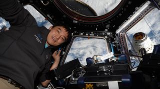 a male astronaut floats inside the international space station with earth in the background