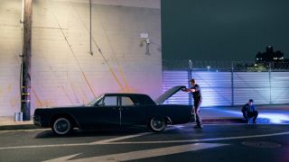 A cop inspecting Mickey's car as he sits on the curb and watches it happen.