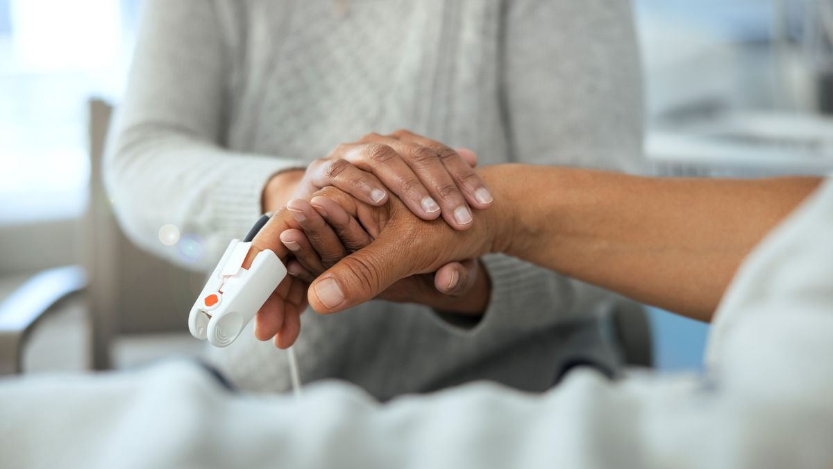 A woman holds a patient&#039;s hands in a hospital bed