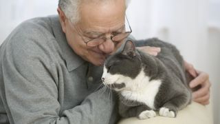 a senior man smiles as he pets his grey and white cat