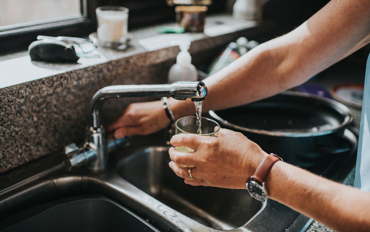 A person filling a glass of water at a kitchen sink