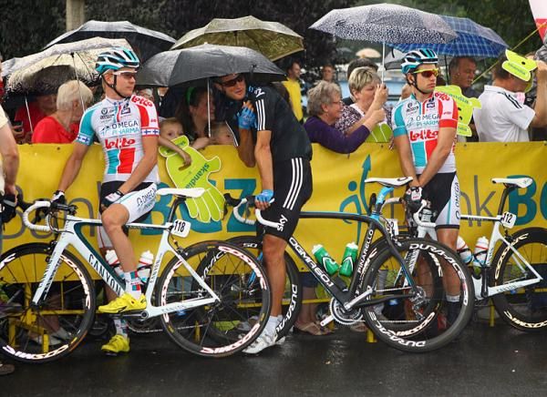 Riders try to stay dry prior to the start of stage three.