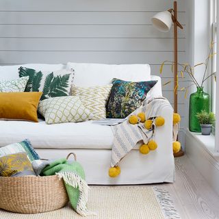 Living room with a white sofa with yellow accents and white wall panels behind