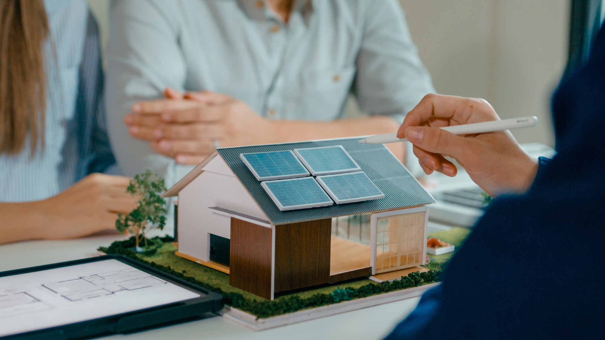 model of contemporary house with solar panels on desk with three people looking at it