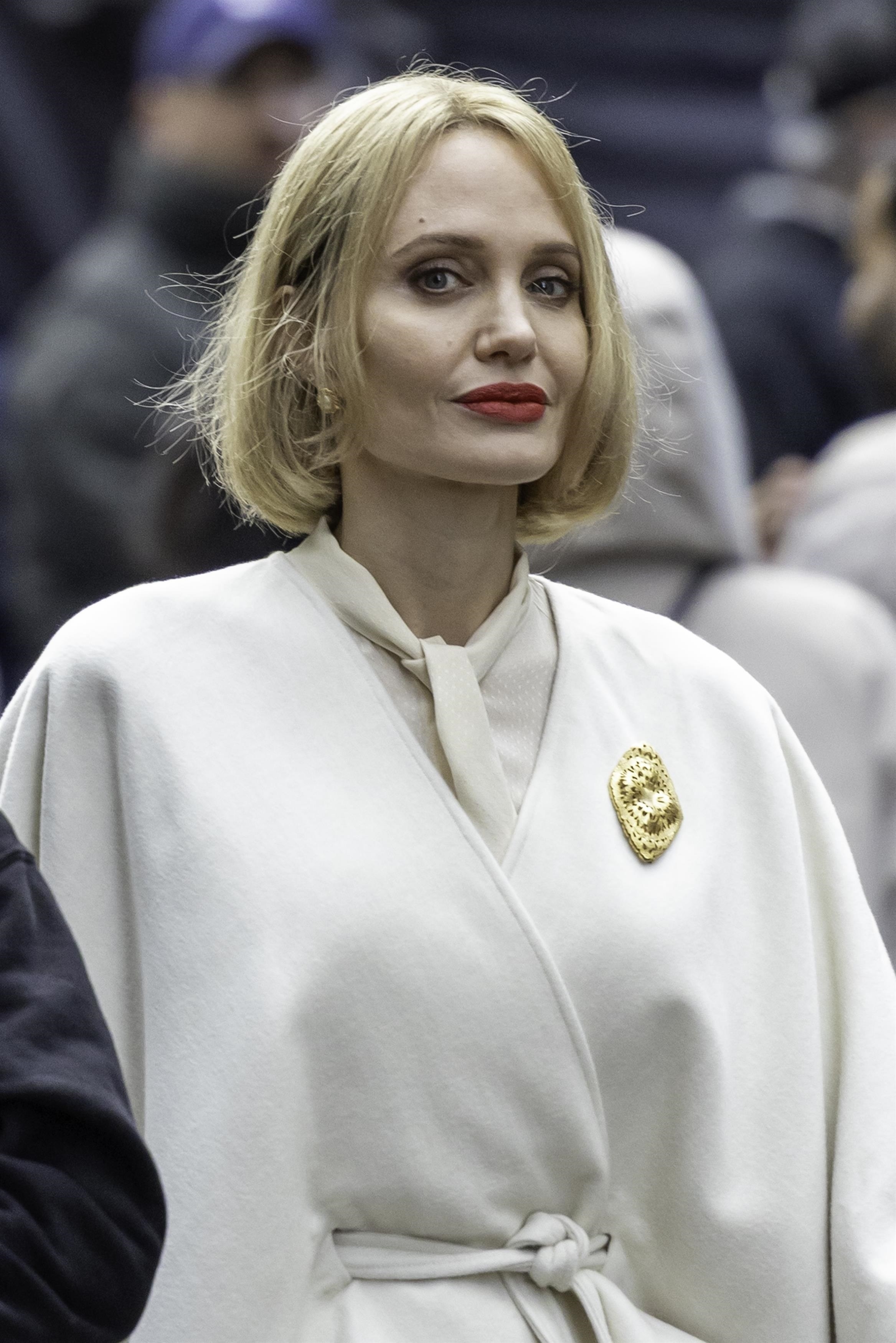 a woman with short blonde hair wearing a cream coat