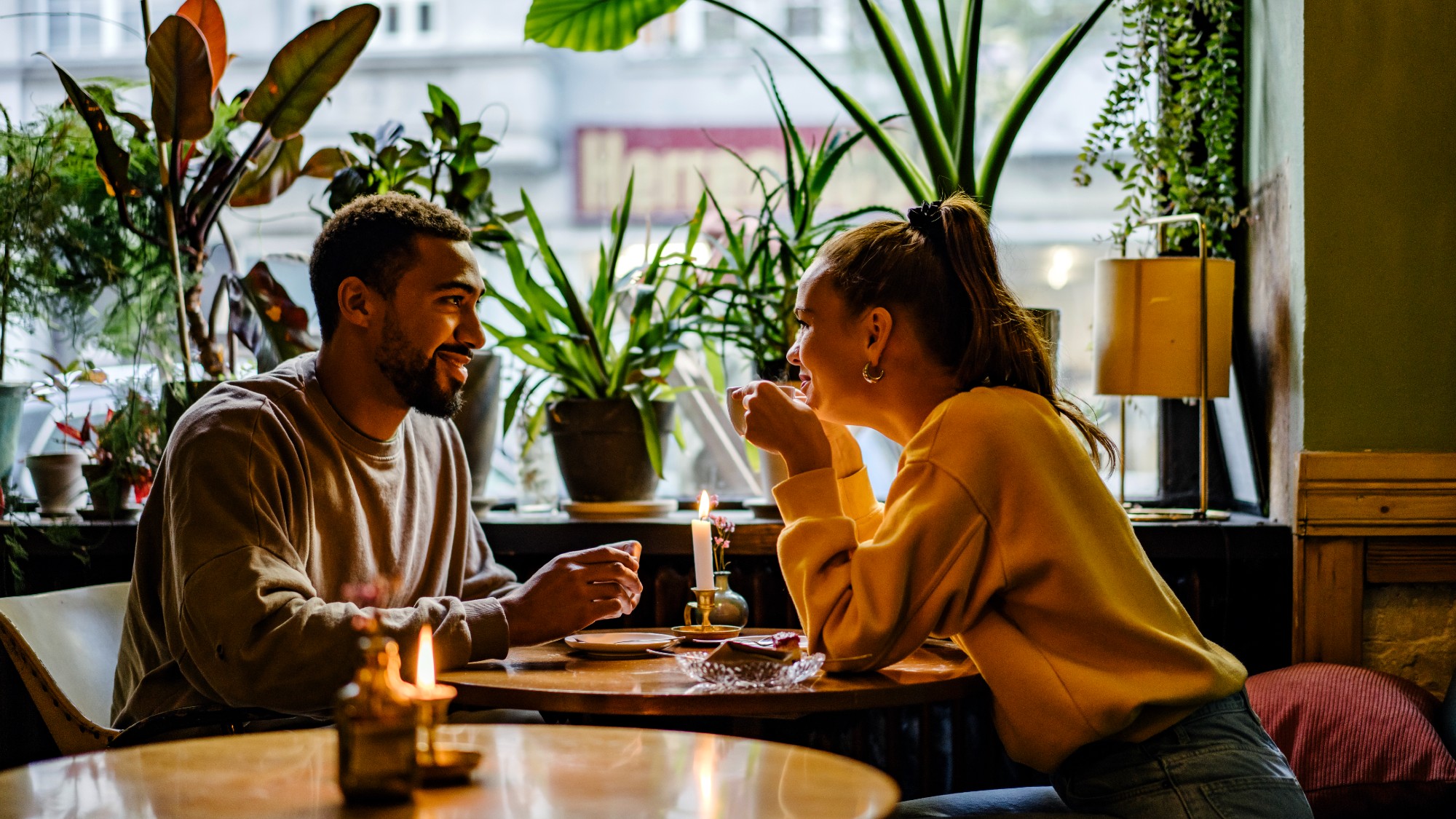 profile shot of a couple sitting at a table by a window of a restaurant. lots of plants are in the windowsill
