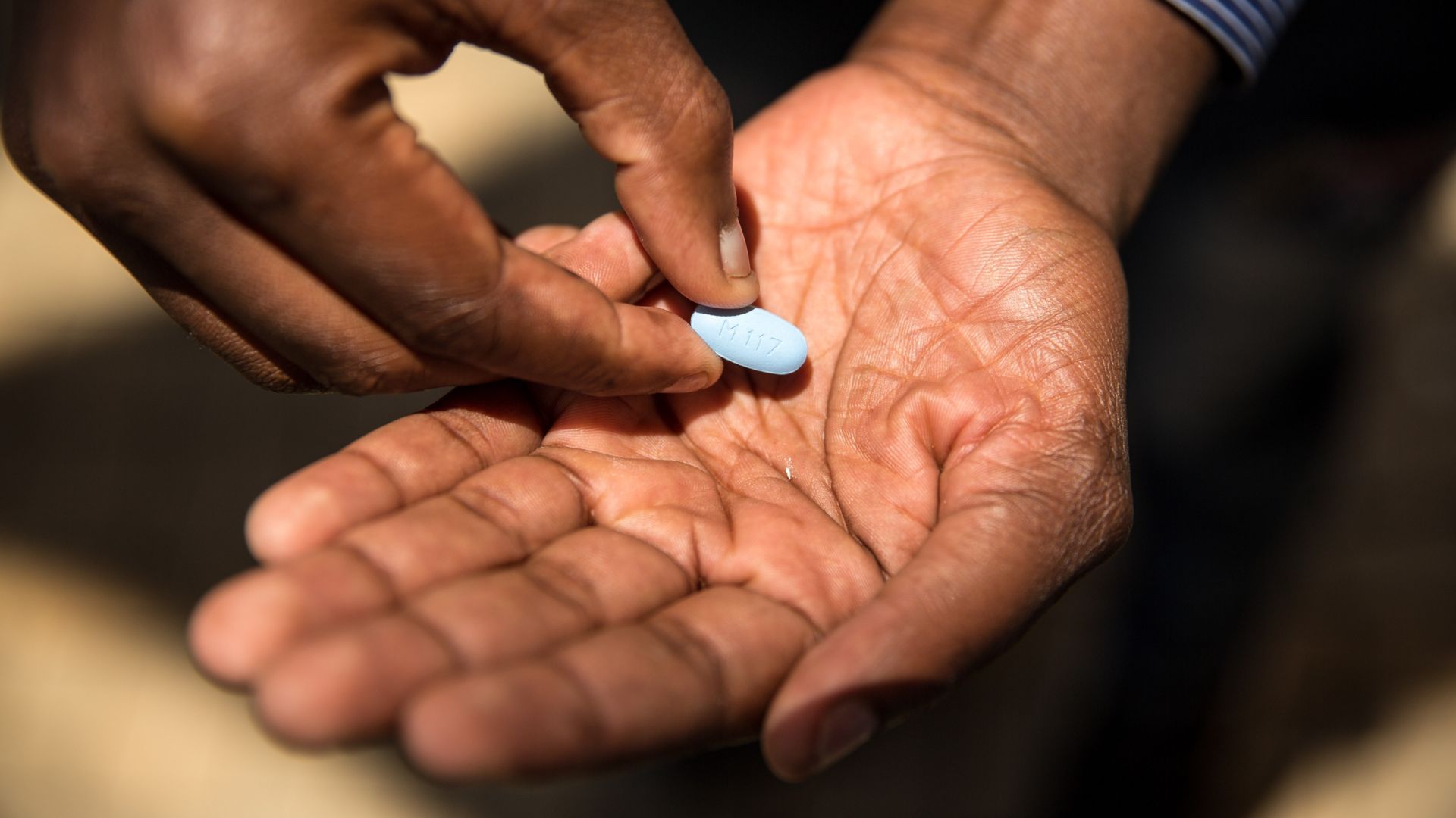 close up of a man's open hand as he places a small, light blue pill onto his palm