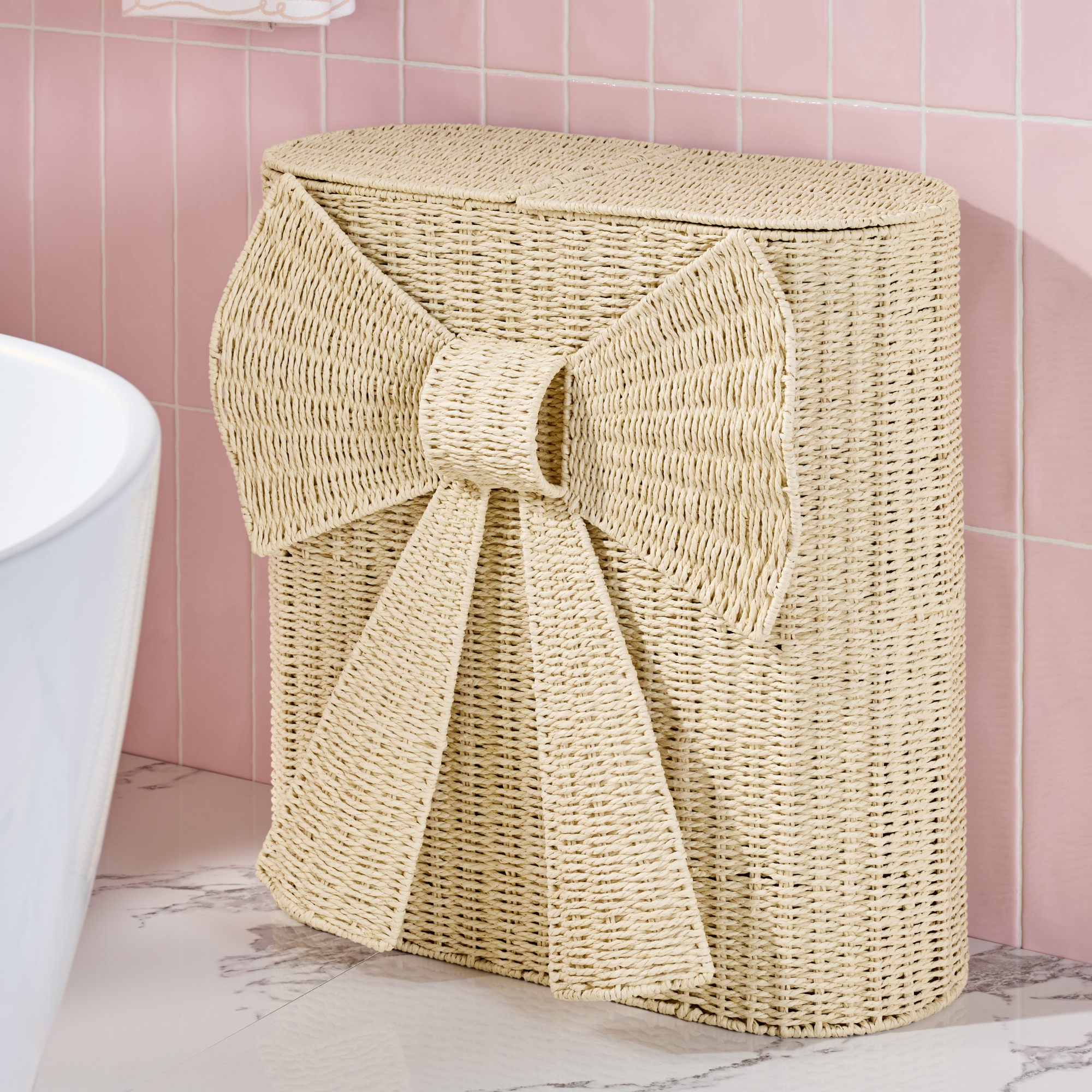 Next natural woven bow laundry sorter in pink tiled bathroom.