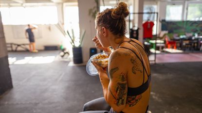 Woman sitting in gym eating from plastic container