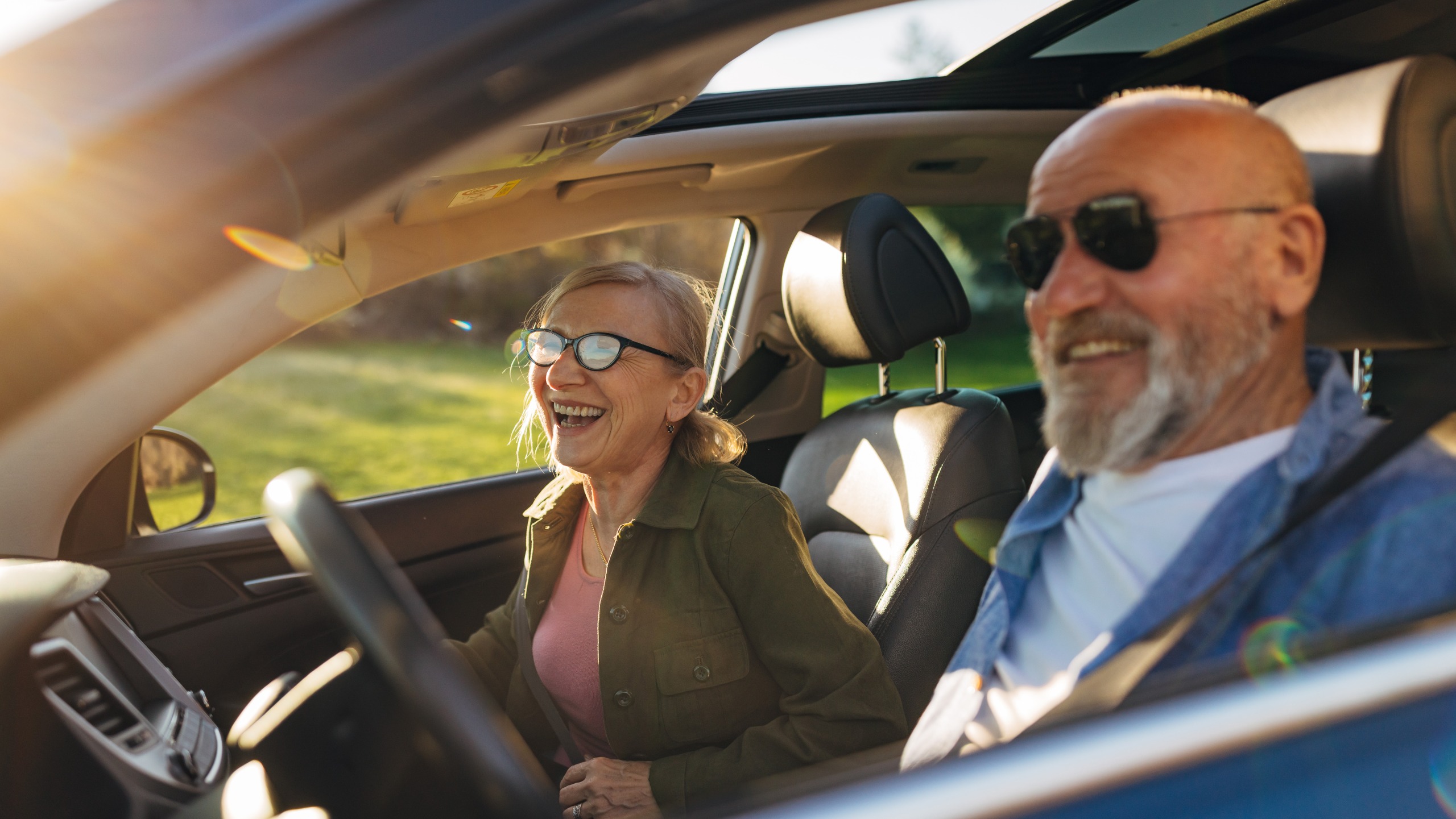 A happy senior couple driving in a car in the countryside.