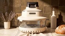An air fryer with a glass mid section, white base, and white lid on a kitchen counter against a green tile backsplash. 