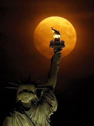 The orange-hued Buck Moon supermoon as seen framed by the Statue of Liberty on July 2, 2023.