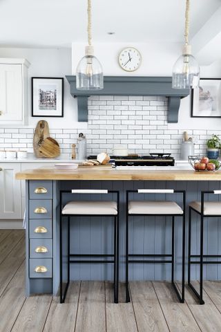 Kitchen with white Shaker-style units, blue island, black metal bar stools and glass pendant lights