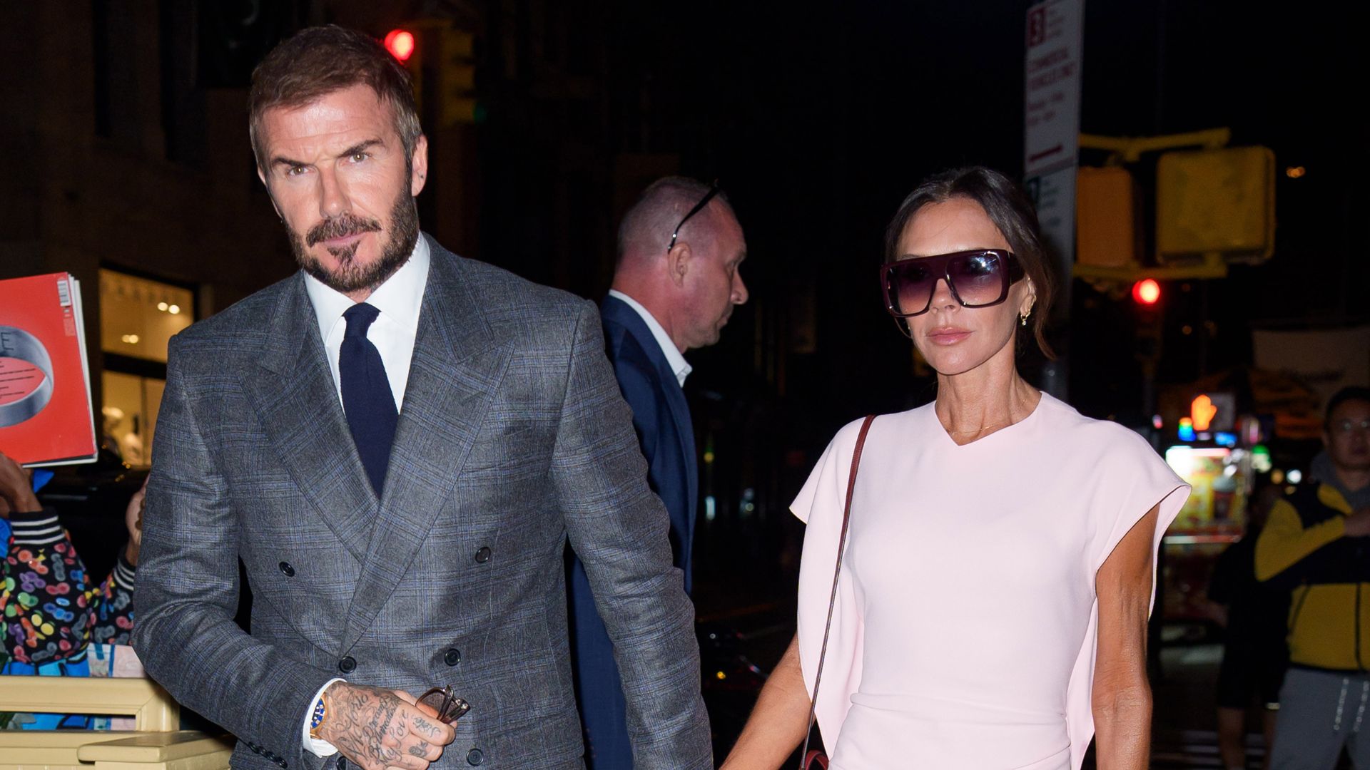 Victoria Beckham hols hands with David Beckham wearing a pink dress, burgundy heels and a burgundy bag.