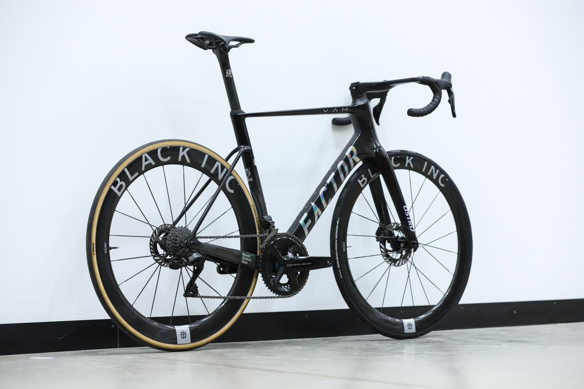 A Black Factor Ostro Vam leans against a white wall