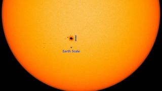 a large sunspot on the surface of the sun with four Earths superimposed over it for scale
