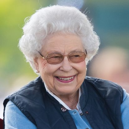 Queen Elizabeth wearing a blue vest and glasses and smiling