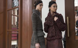 Two women in a wooden doorway. One wearing a black and white houndstooth jacket and skirt, and the other in a maroon jacket and skirt