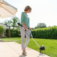 Woman cutting edges of a lawn beside a patio using a Bosch strimmer