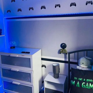 a boys room with a black framed bed, white chest of drawers, neon string lights and gaming controller stickers on the wall