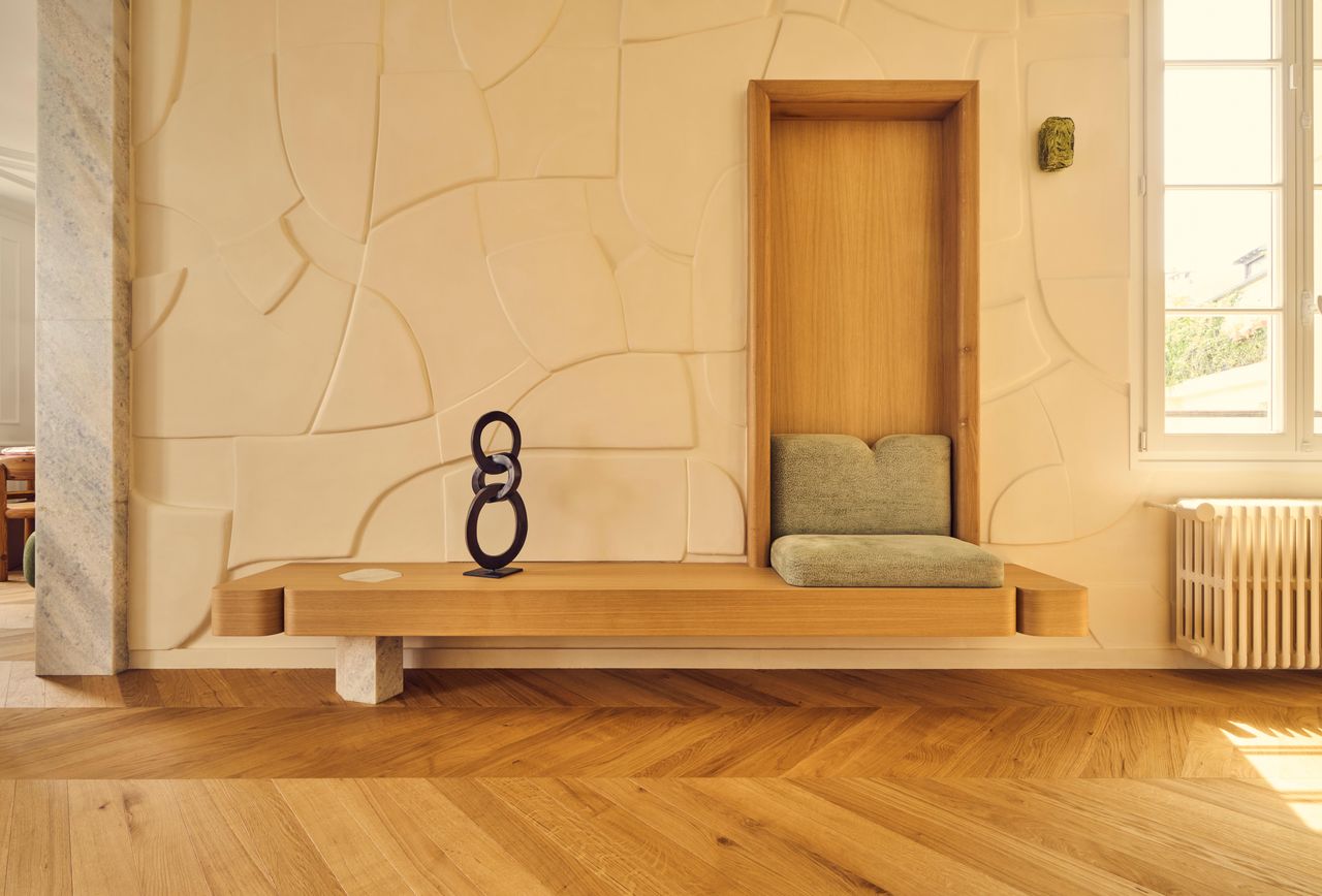 Batiik Studio-designed apartment entryway featuring an antiqued mirror ceiling, herringbone floors, and a sculptural bench with green cushions