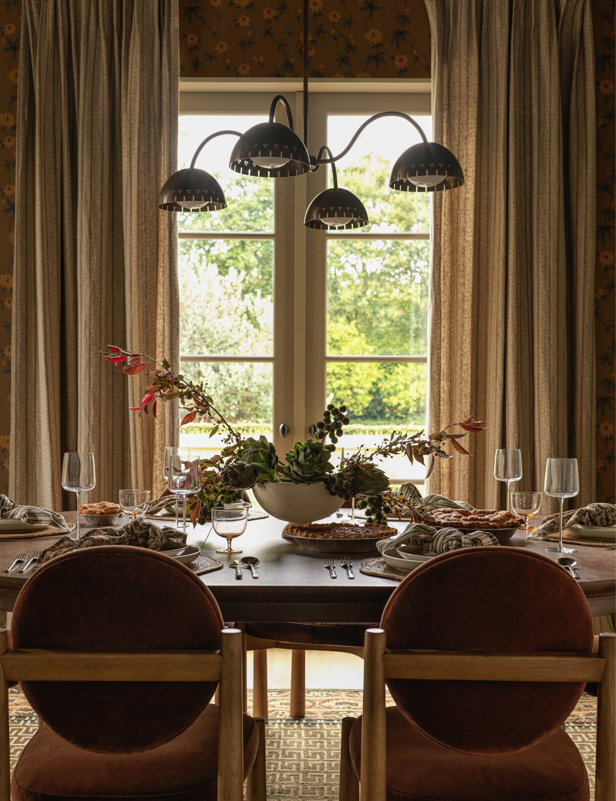 Whimsically modern fall table by Lulu and Georgia, featuring an artichoke centerpiece, mid-century dining chairs, and a sculptural chandelier overhead.
