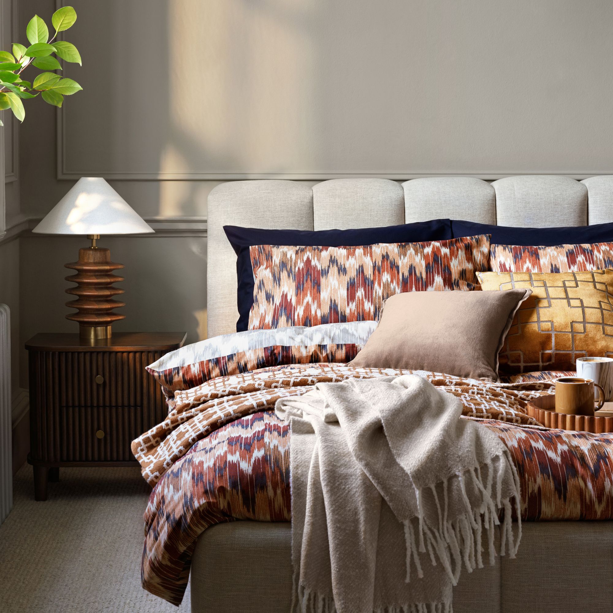 A modern luxe bedroom with light grey walls and a curved bed with layered bedding