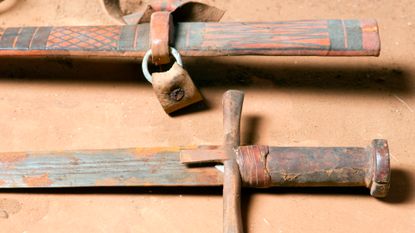 A close of up a rusty sword with a brown hilt and its brown, leather scabbard.