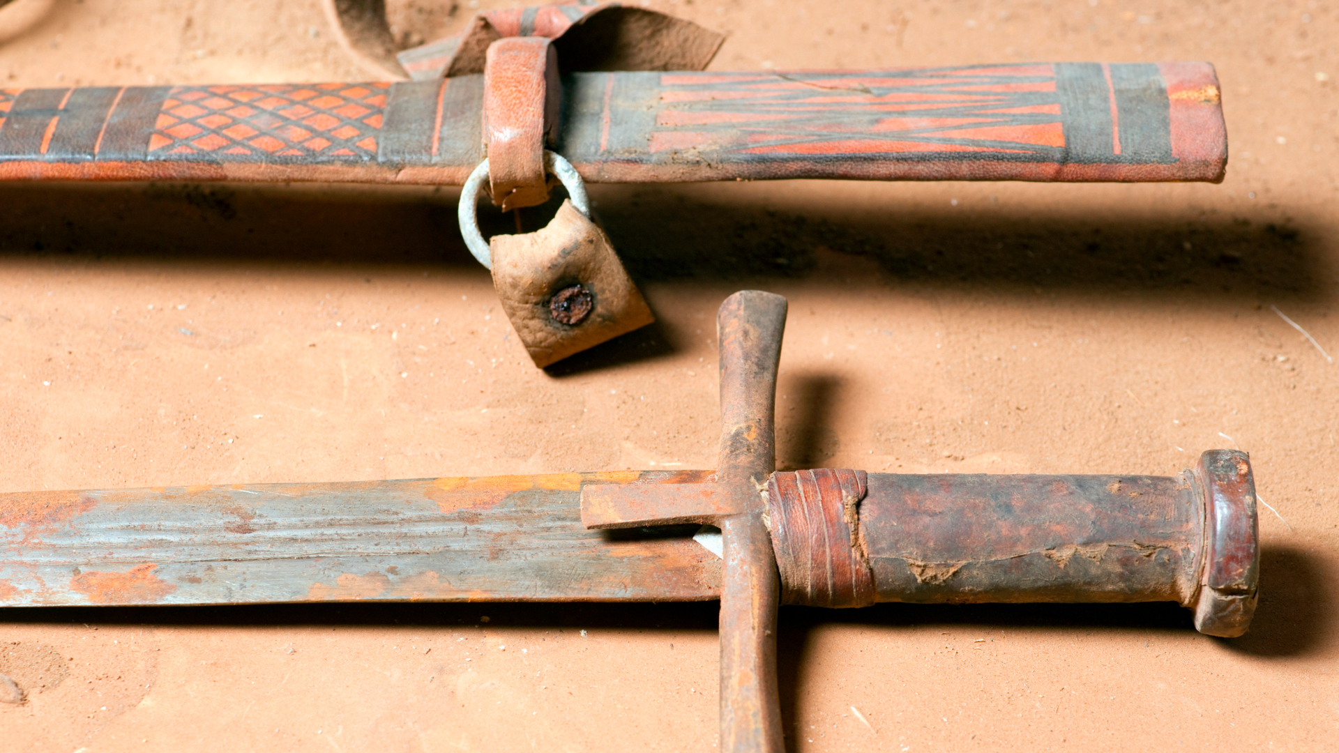 A close of up a rusty sword with a brown hilt and its brown, leather scabbard.