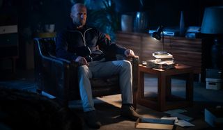 Jason Statham sits in a darkened living room in Wrath of Man.