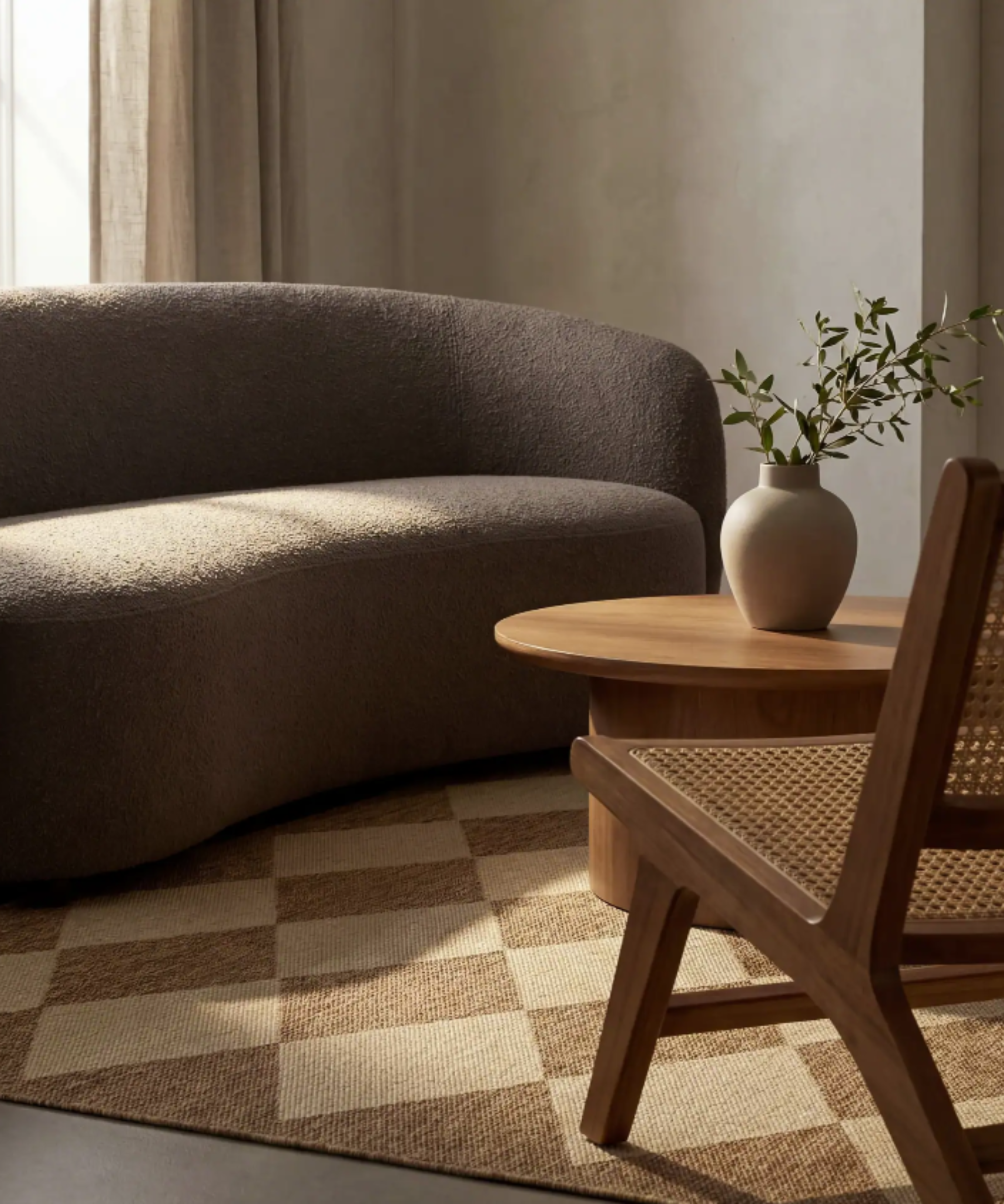 Neutral living room featuring a curved mocha sofa, circular wooden coffee tale, and cane accent chair, lined by a harlequin diamond tan-on-beige rug from Rugs USA.