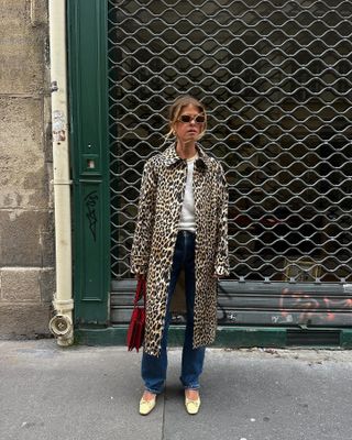 Paris woman wears a Rouje leopard print trench coat with yellow ballet flats and a red purse.
