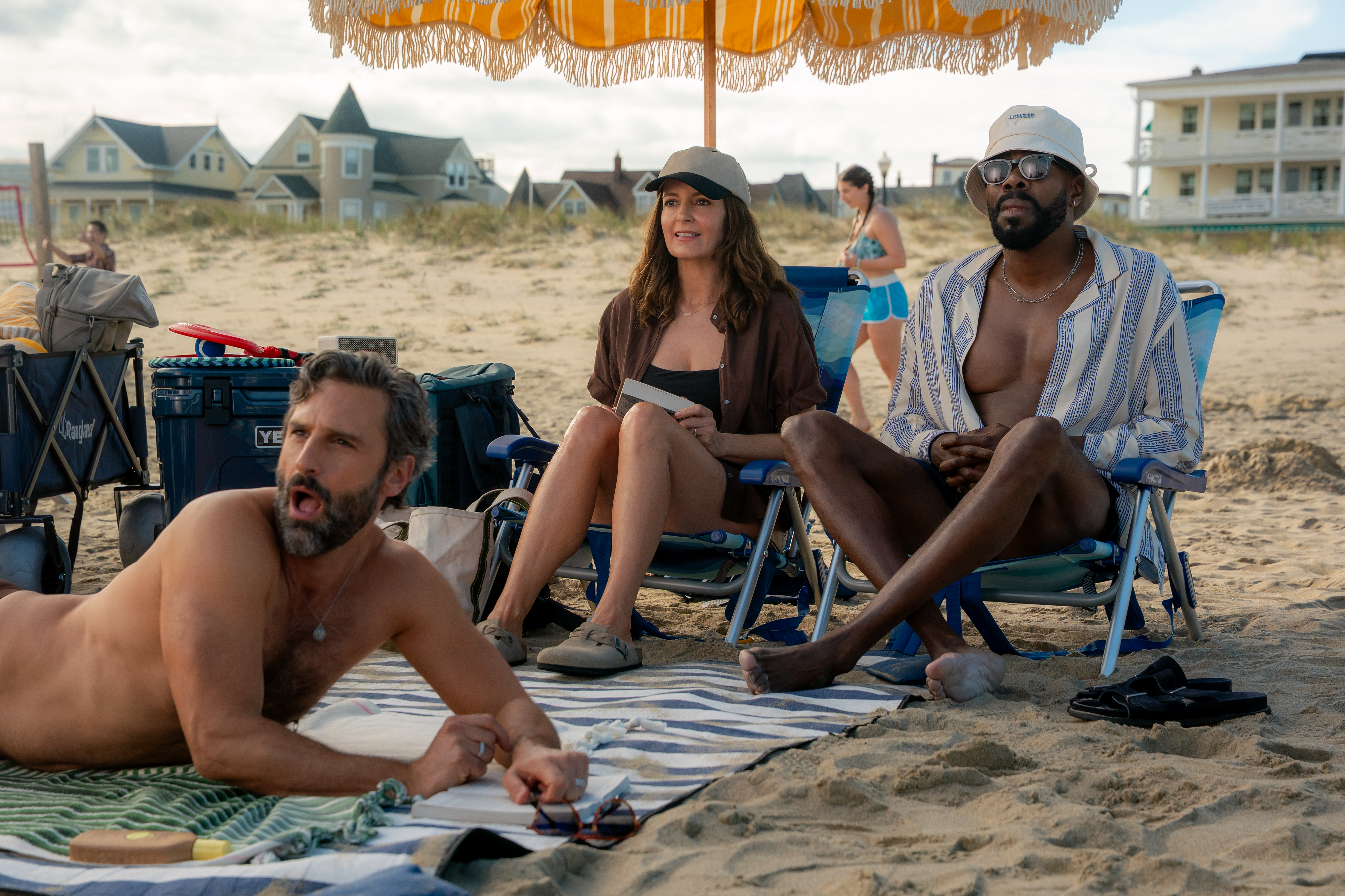 Marco Calvani as Claude, Tina Fey as Kate, and Colman Domingo as Danny sitting on lawn chairs and a towel on the beach at the jersey shore in the four seasons