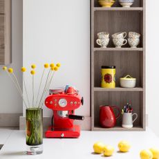 White kitchen with wooden shelves filled with mugs, and a red coffee machine on a white worktop