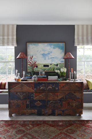 Wooden chest of draws with blue and red hand painting design, red patterned rug and matching lamps