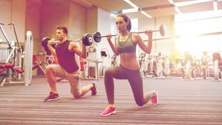 Man and woman perform lunge holding barbells across their shoulders