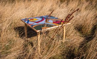 Wooden square table with colourful top photographed in a meadow