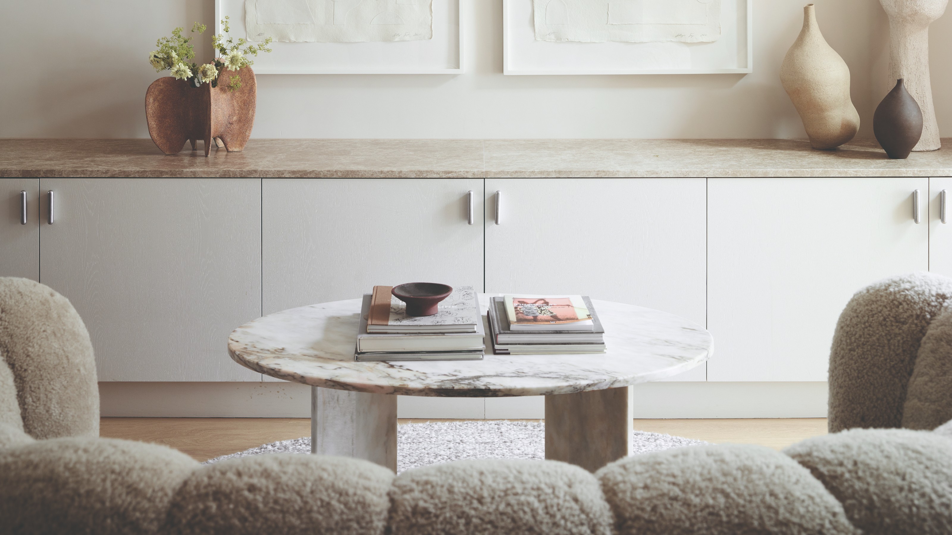 A white living room with a round marble coffee table and a curved boucle sofa