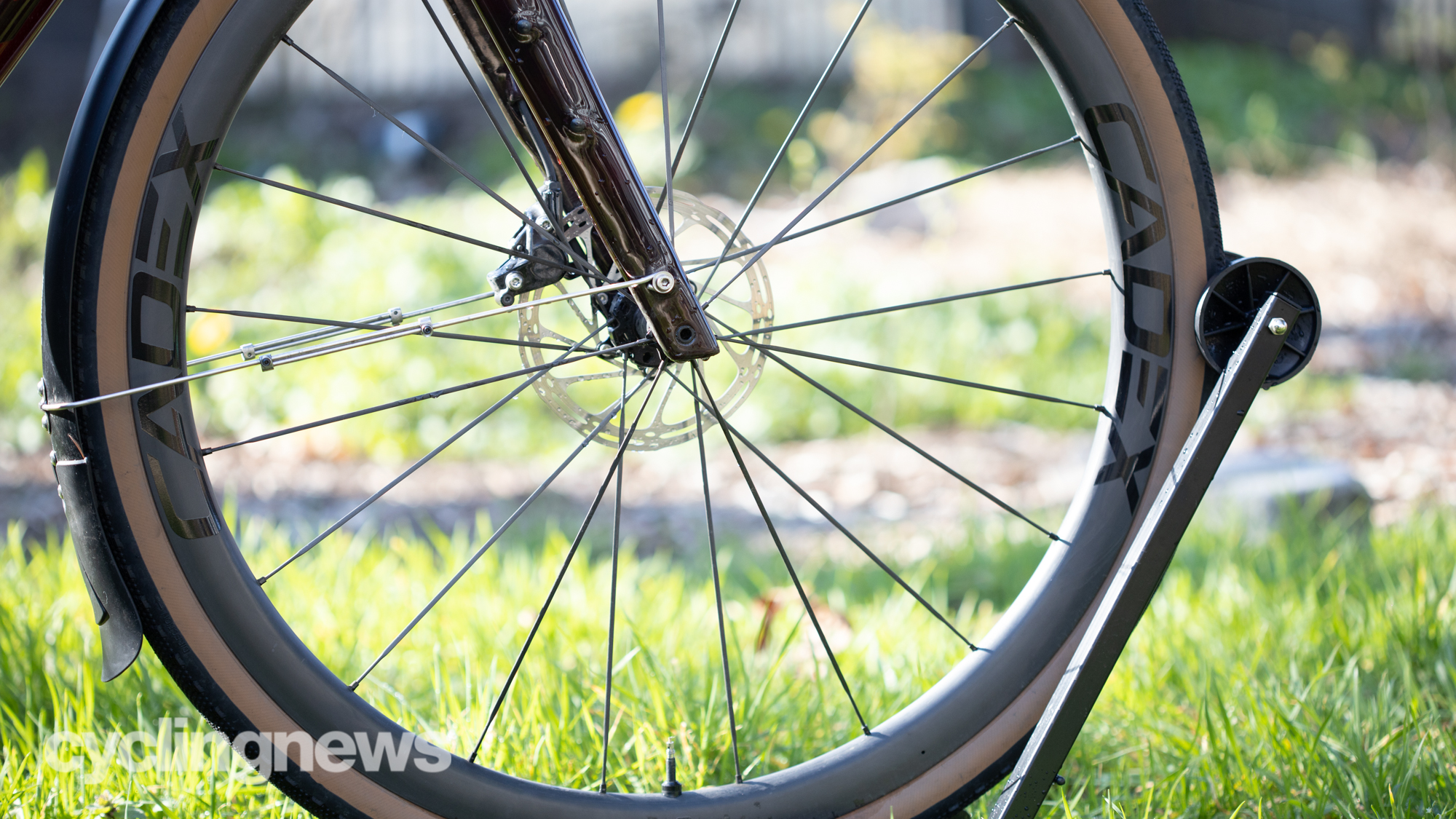 The front Cadex wheel and forks of a bike, held up in a stand on some grass