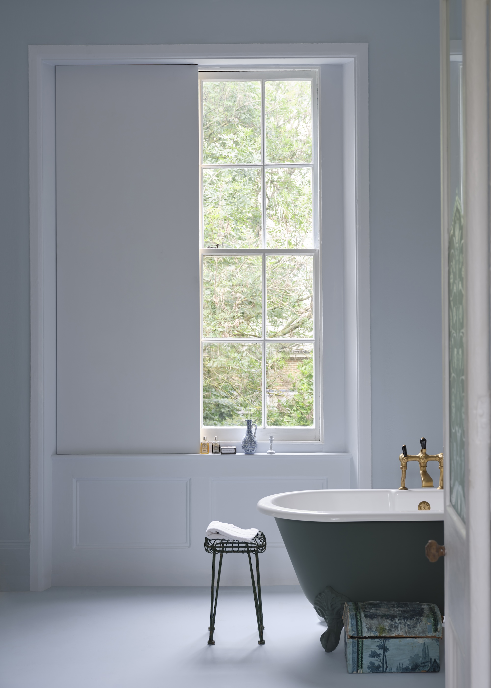 A classic light filled bathroom with dusty blue walls and a freestanding roll top bath