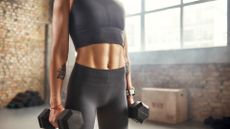 Woman holding two dumbbells in a studio showing abs muscles