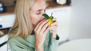 Young woman with blonde hair sniffing a fresh tangerine at her kitchen table