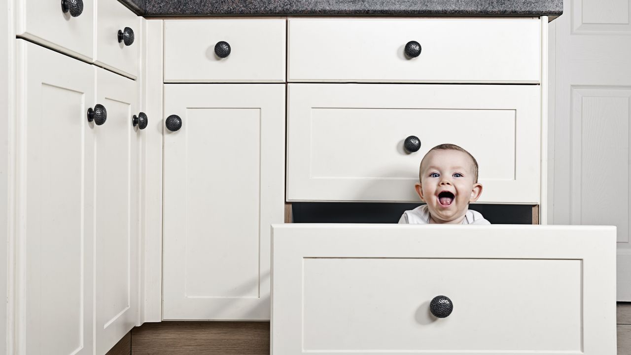 A happy baby sits in on open kitchen drawer.