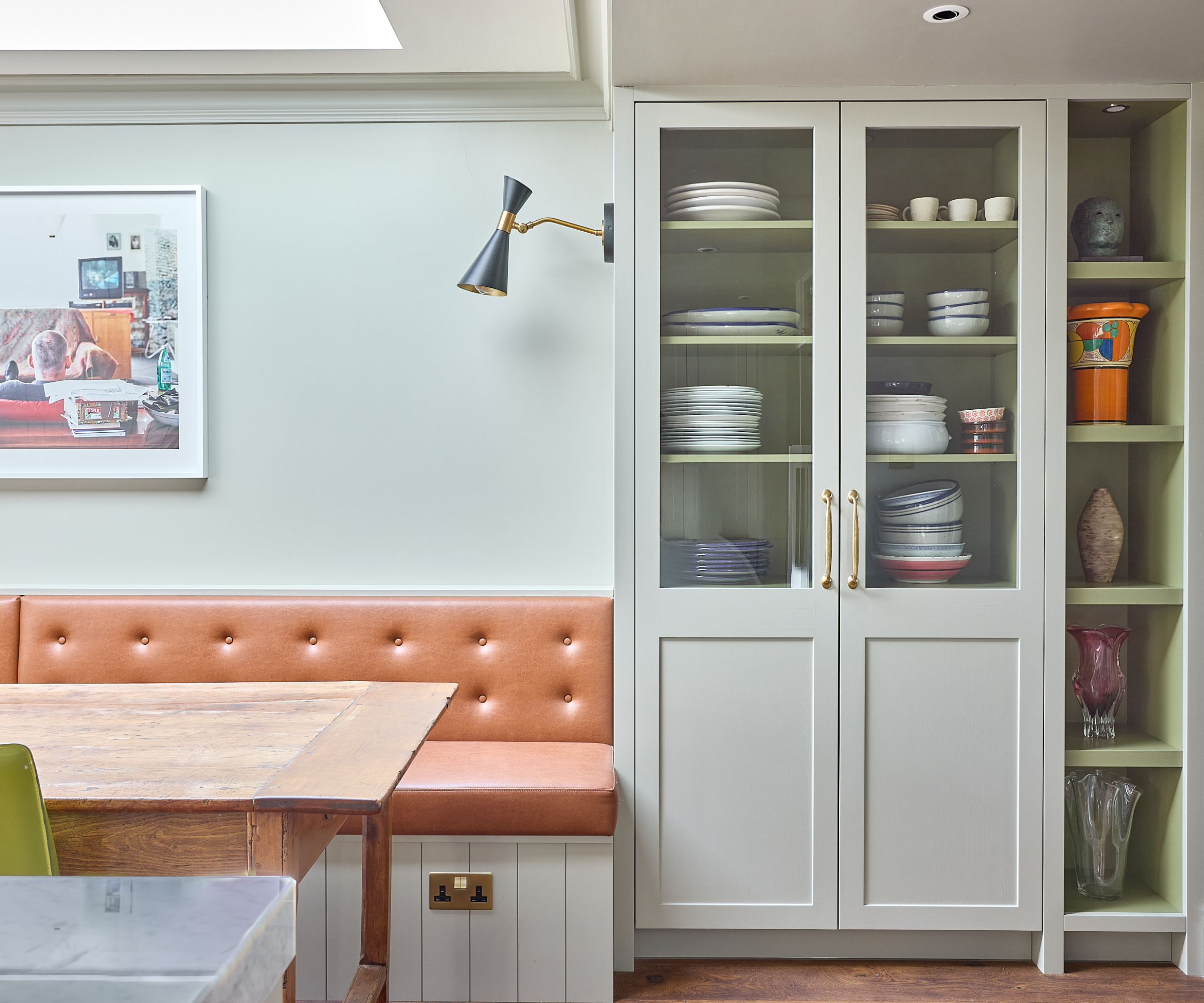 kitchen painted in soft green with brighter green shelves, pale terracotta banquette seating