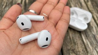 Apple AirPods 4 with ANC wireless earbuds held in palm of hand above wooden table