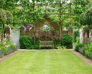 An example of how to landscape a backyard showing a square lawn with paths on each side and a wooden bench next to a brick wall