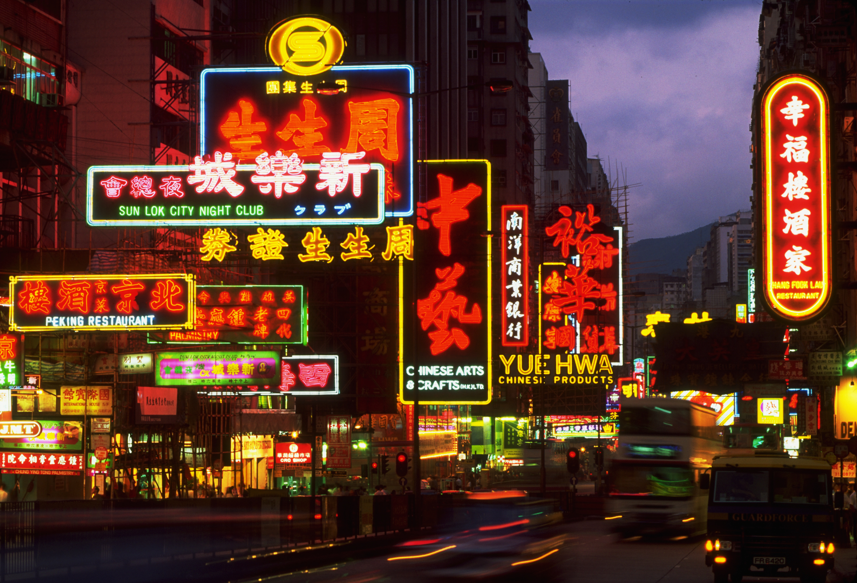 A nightlife scene of Hong Kong, with neon-lit signages and racing cars against a pink-hued sky.