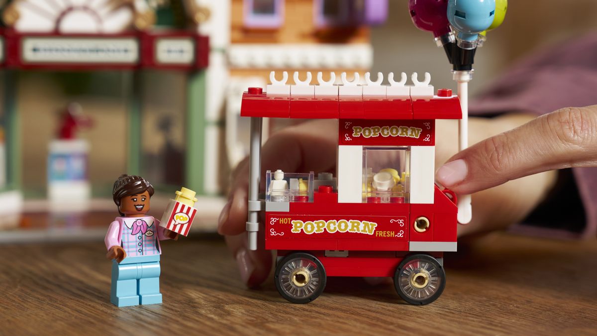 A finger pushes the Main Street USA Popcorn stand beside a minifigure