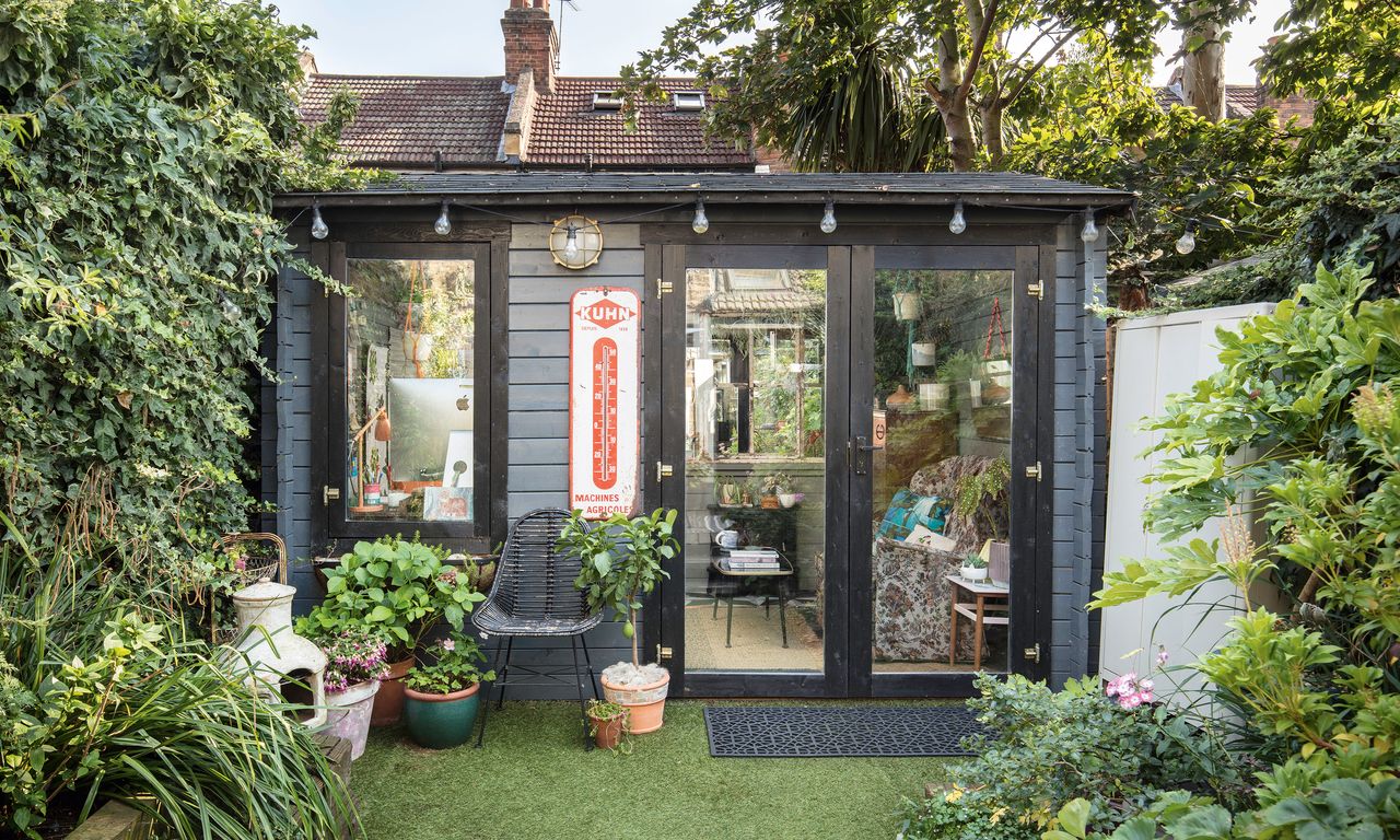 Garden room summer house painted black with wood panelling, festoon lights and pot plants